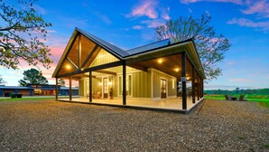 A modern, open-plan building with a large glass facade, outdoor seating area, and a gravel driveway.