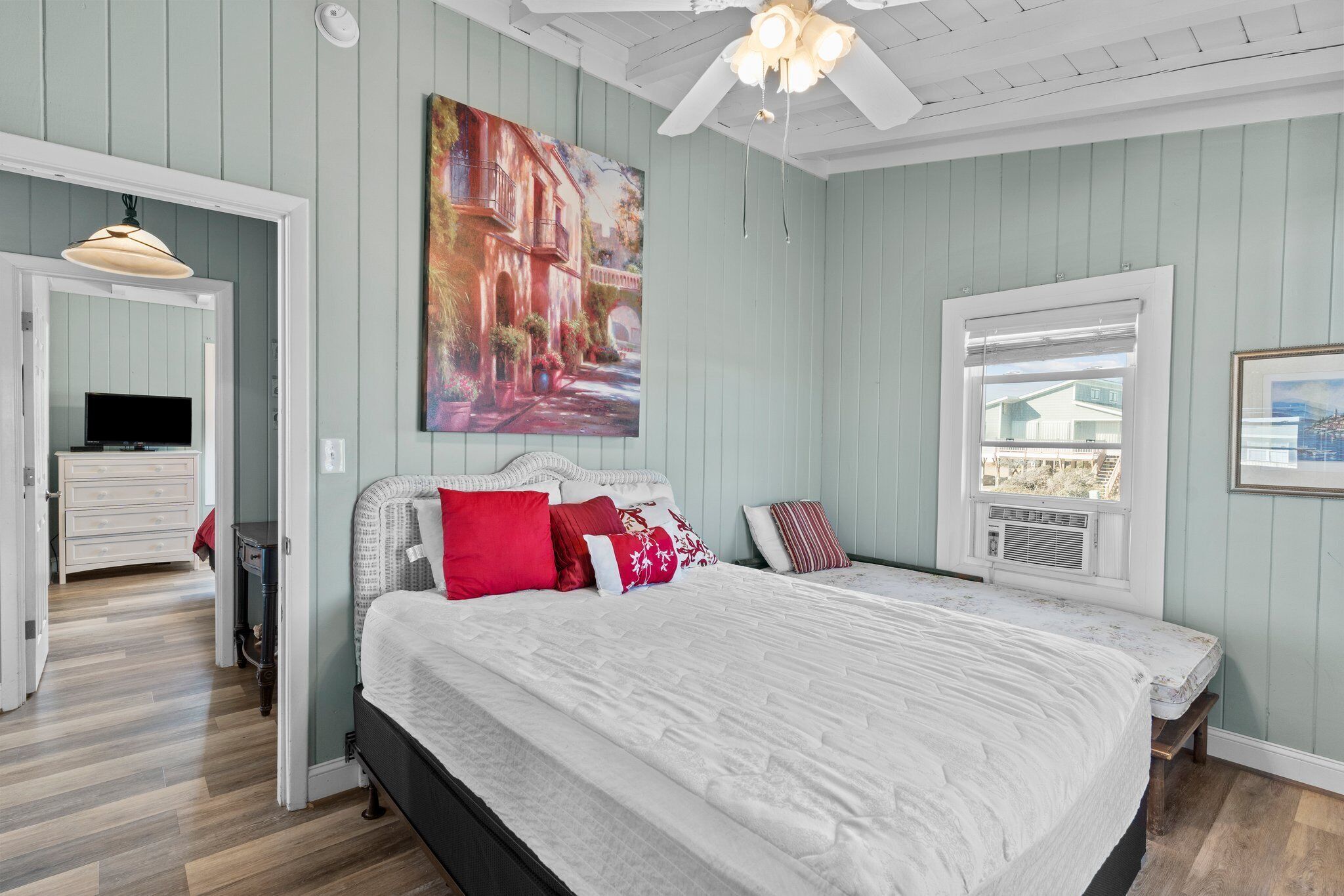 Quarto com cama, quadro, ventoinha no teto e janela.