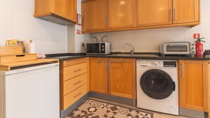 Uma cozinha compacta com armários de madeira, micro-ondas, torradeira, máquina de lavar e um frigorífico pequeno.