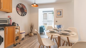 Uma cozinha com micro-ondas, armários de madeira, um relógio e um espaço de jantar com mesa posta para dois.