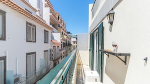 Uma rua estreita ladeada por edifícios, com um corrimão verde e uma parede branca com uma taça e garrafa de vinho.