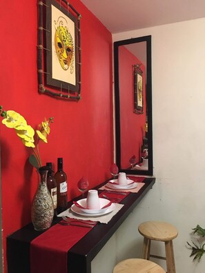 A dining area with a red wall, a mirror, a vase with yellow flowers, and a wooden stool. - Abboud Staycation  (Manila)