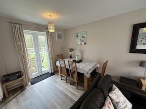 Un salon comprenant un canapé, une table à manger avec des chaises, un téléviseur posé sur un meuble et une porte donnant sur un balcon.