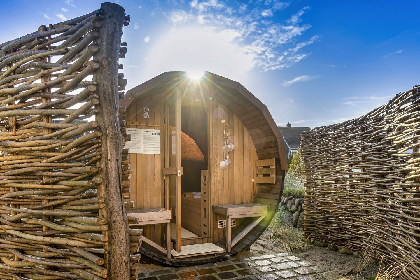 Una sauna in legno con tetto curvo, ingresso in legno e un vialetto in pietra che vi conduce.