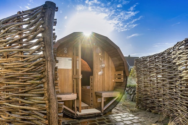 A wooden sauna structure with a curved roof, a wooden entrance, and a stone pathway leading to it.