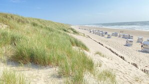 Une plage avec des dunes de sable et une rangée de cabanes de plage numérotées.