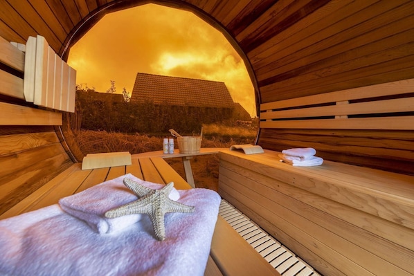 A sauna with wooden benches, a starfish towel, and a bucket with bottles, viewed through a circular opening.