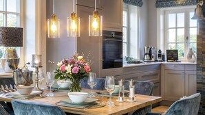 Une cuisine moderne avec un coin repas, comprenant une table en bois dressée pour six personnes, un vase de fleurs et des lampes suspendues.