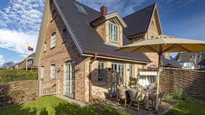 Une maison en briques avec un toit en pente, une terrasse avec des meubles d’extérieur et un drapeau en arrière-plan.