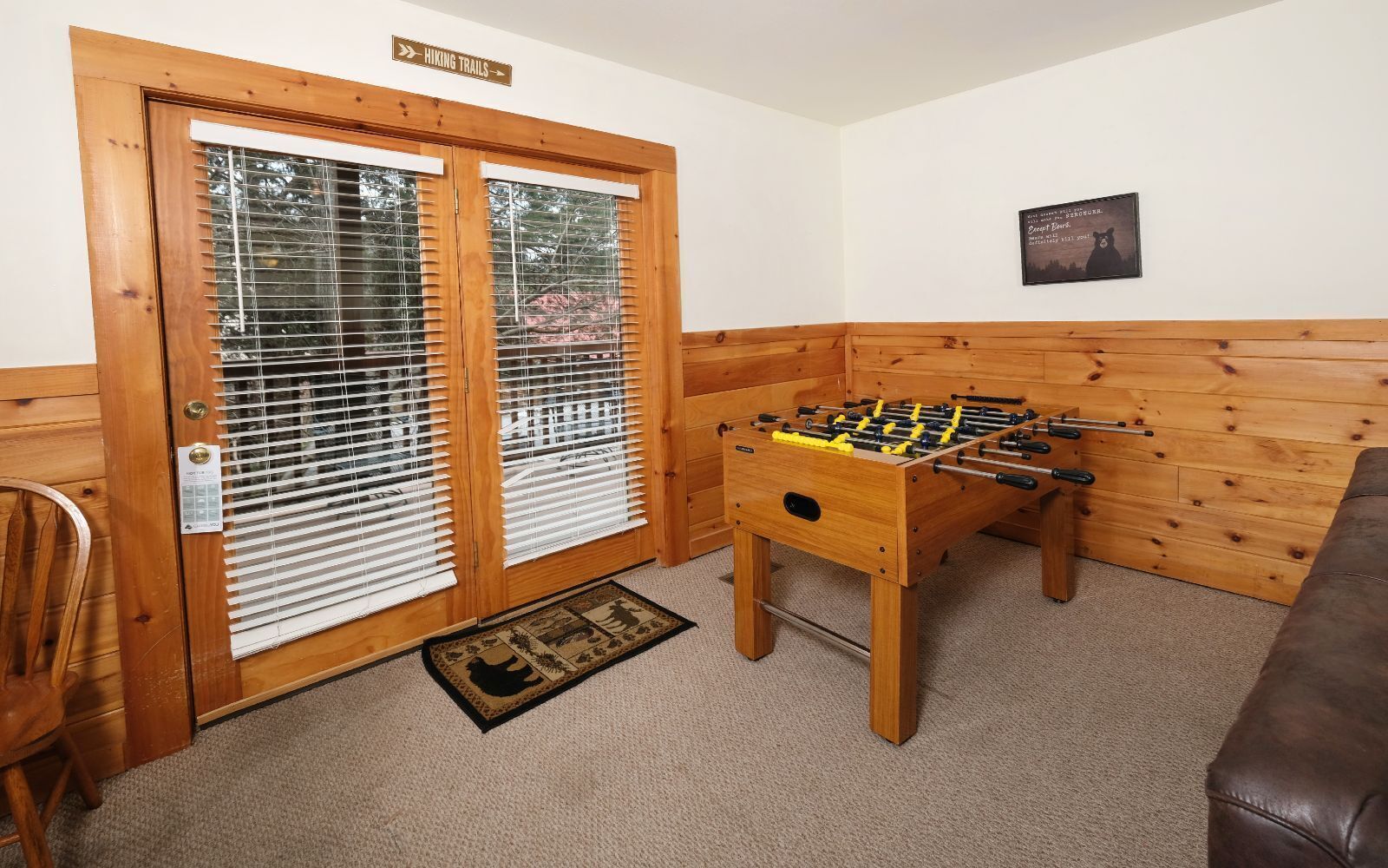 A cozy room with a wooden door, a foosball table, and a brown leather couch.