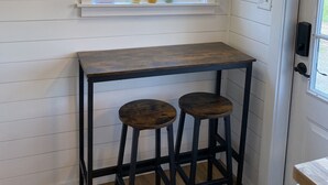 A kitchen with a window, a wooden ceiling, and a bar stool. - The Arkansas Tiny House (Mulberry)