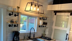 A modern kitchen with white cabinets, a wooden countertop, a built-in stove, and a window overlooking the backyard. - The Arkansas Tiny House (Mulberry)