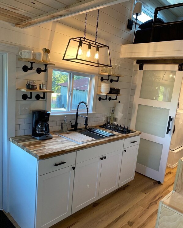 Kitchen features a central island with sink, coffee maker, and utensils, plus a unique light fixture and cabinetry.