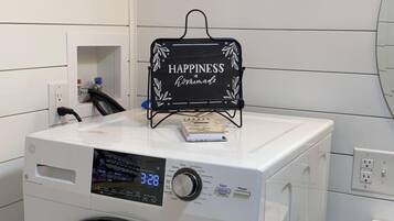 A front-loading washing machine with a digital display, a small shelf with a sign, and a white tiled wall.