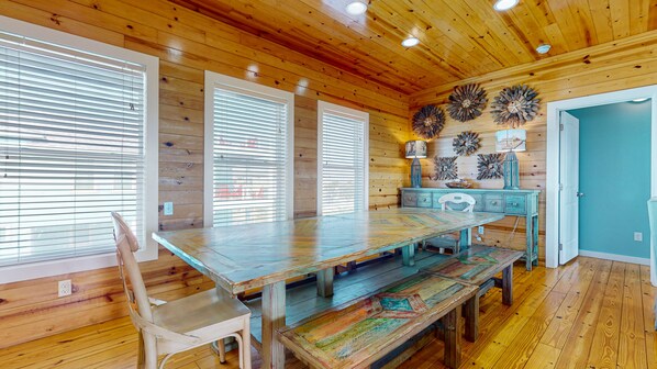 A wooden interior with a large dining table, chairs, and a blue door.
