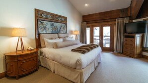 A bedroom with a large bed, a wooden dresser, a lamp, a painting, a television, and a sliding glass door to a balcony. - Luxury King Room Hotel Room by RedAwning (Park City)