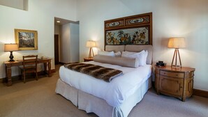 A hotel room with a large bed, two bedside lamps, a desk with a chair, a painting on the wall, and a wooden nightstand. - Luxury King Room Hotel Room by RedAwning (Park City)