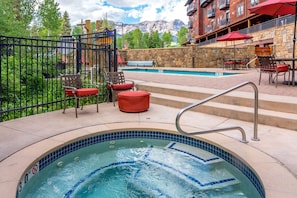 Relax by the serene pool surrounded by lush greenery and a stone wall, with a hot tub and comfortable seating areas.