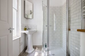 A bathroom with a white pedestal sink, a glass shower enclosure, and a mirror on the wall.