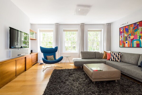 A modern living room with a flat-screen TV, a blue chair, a grey sofa, and a black rug.