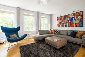 A modern living room with a blue chair, grey sofa, and a black rug.