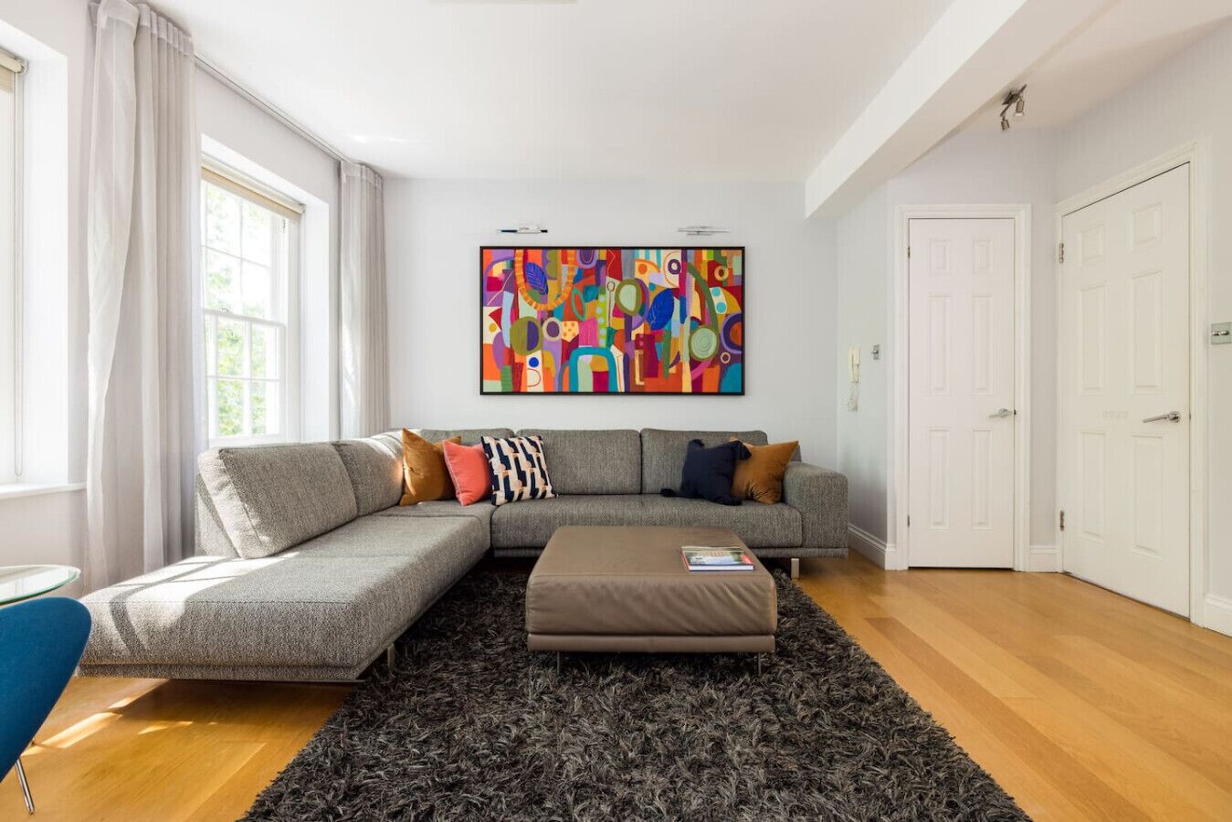 Una sala moderna con un sofá modular, una mesita de centro y un cuadro abstracto lleno de color.