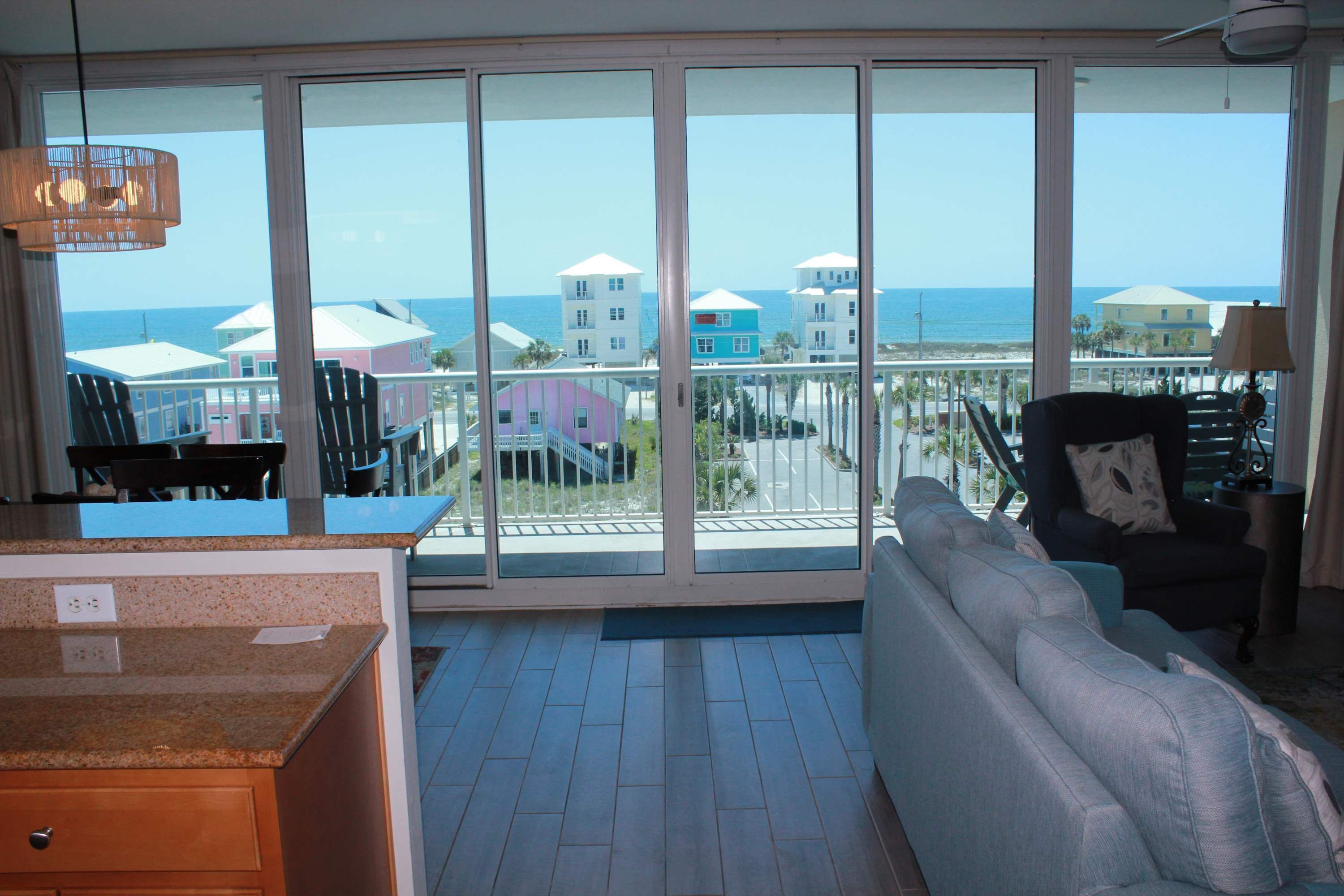 A spacious living area with a large sliding glass door leading to a balcony with a view of the ocean and colorful buildings.