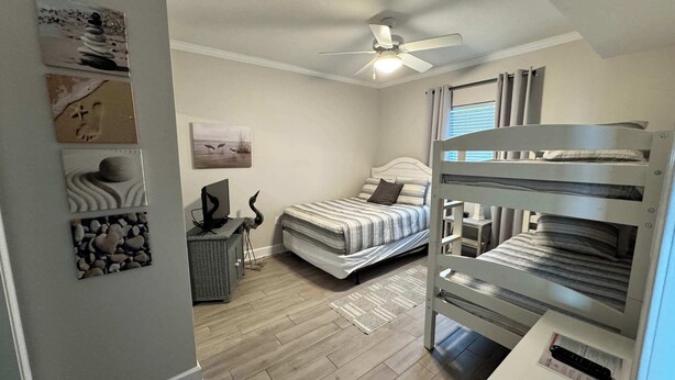 Un dormitorio con cama, escritorio, silla, ventilador de techo y una obra de arte en la pared.