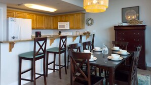 Una cocina con armarios de madera, un microondas y un comedor con una mesa preparada para cuatro.
