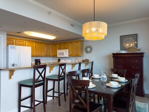 A kitchen with wooden cabinets, a microwave, and a dining area with a table set for four. - Sanibel 406 by ALBVR - Beautiful updates with views that are simply amazing! (Gulf Shores)