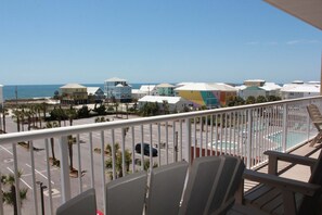 A balcony with chairs overlooking a parking lot and colorful buildings near the beach. - Sanibel 406 by ALBVR - Beautiful updates with views that are simply amazing! (Gulf Shores)