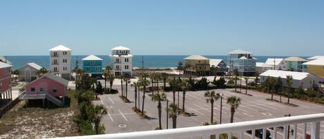 A coastal view of a parking lot with several buildings, including a pink house and a blue building with a white roof, near the beach.