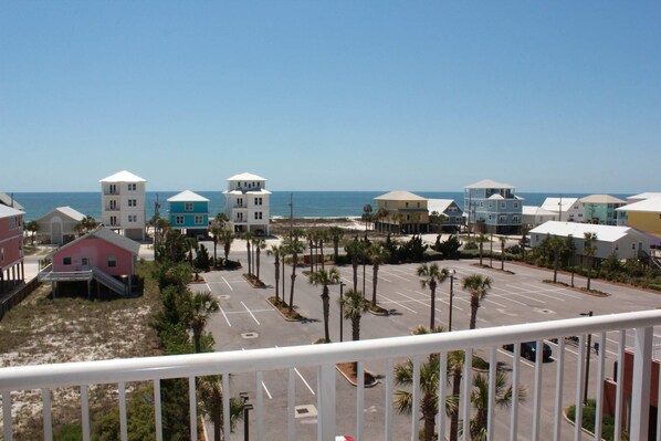 A coastal view of a parking lot with several buildings, including a pink house and a blue building with a white roof, near the beach.