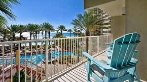 A balcony with a pool, lounge chairs, and a view of the ocean and palm trees. - Shores Of Panama 314 - 1 Bd+bunks, Sleeps 6. Same Level Parking, Free Fun! 1 Bedroom Condo by RedAwning (Panama City Beach)