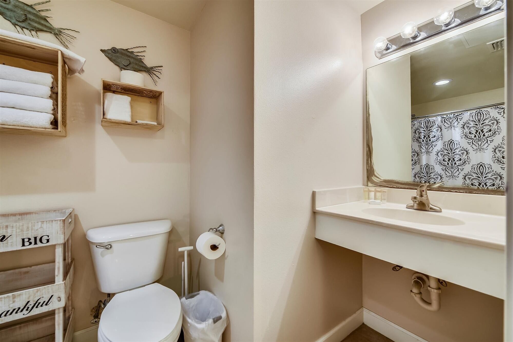 A bathroom with a toilet, sink, and mirror. There are towels and a trash can visible.