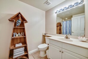 Un baño con un toallero de madera, un lavamanos, un inodoro y un espejo con iluminación superior.