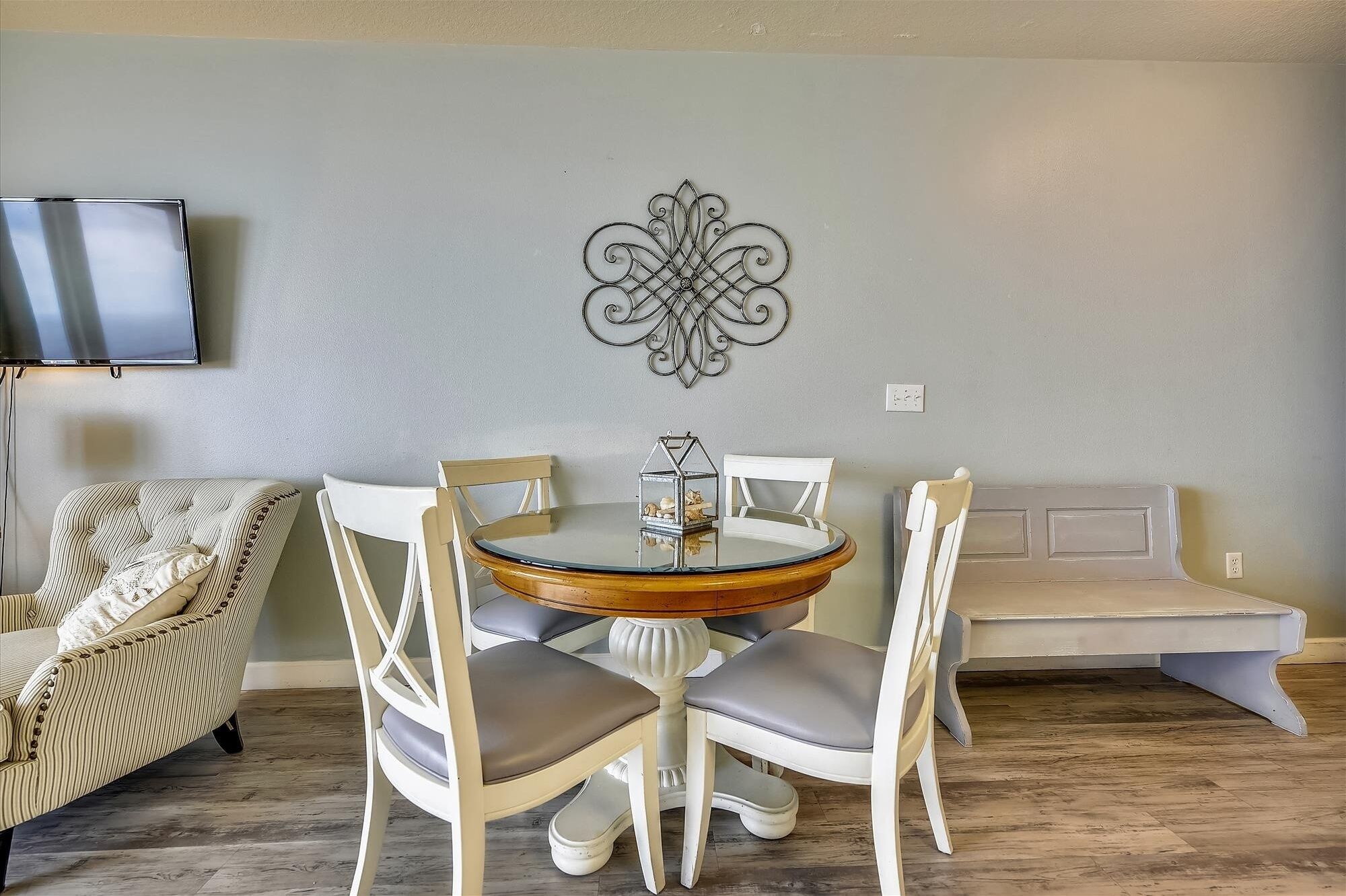 Un coin repas comprenant une table ronde, des chaises blanches, un élément décoratif mural, un téléviseur et un canapé.