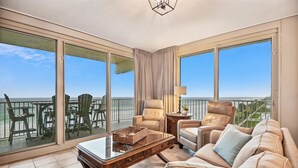 Un balcon spacieux offrant une vue sur la plage, aménagé avec un canapé, des fauteuils et une table à plateau en verre.