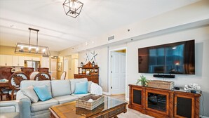 Un salon comprenant un canapé, une table basse, un téléviseur, un meuble en bois et un coin repas avec des chaises et une table.