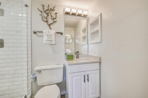 Bathroom features a white tiled shower area, toilet, vanity with sink and mirror, and decorative wall art.