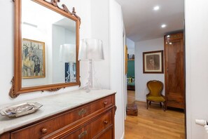 Une pièce comprenant une commode en bois, un grand miroir, une lampe et une chaise.