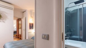 A bedroom with a bed, a bathroom with a shower, and a door leading to another room. - Auditorium Roof Top Apartment (Roma)
