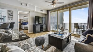 A spacious living room with a large TV, comfortable seating, a ceiling fan, and a balcony with a view of the city. - Shores of Panama 1011 - 1 Bedroom+Bunks . Free Fun! 1 Condo by RedAwning (Panama City Beach)
