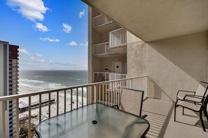 A balcony with a glass table and chairs, overlooking a beach and ocean.