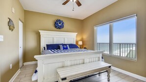 A bedroom with a bed, a ceiling fan, a window with a view, and a bench. - Shores of Panama 1804 - 2 Bedroom + Bunkroom . Updated! Free Fun. 2 Condo by RedAwning (Panama City Beach)