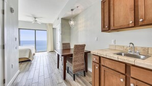 A spacious kitchen with wooden cabinets, a dining area with wicker chairs, and a view of the ocean through a sliding door. - Origin at Seahaven 1036/1038 - 2 Bedroom Unit 2 Home by RedAwning (Panama City Beach)