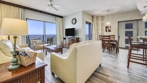 A spacious living room with a balcony, a television, and a dining area with wooden furniture. - Origin at Seahaven 1036/1038 - 2 Bedroom Unit 2 Home by RedAwning (Panama City Beach)