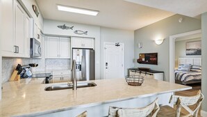 A modern kitchen with white cabinets, a stainless steel refrigerator, and a large island with a sink. - Gulf Crest 2005 - 2 Bedroom W/Fantastic View! Family Friendly! Sleeps 8 Condo by RedAwning (Panama City Beach)