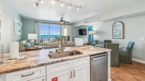 A modern kitchen with a large island, a ceiling fan, and a view of the ocean.
