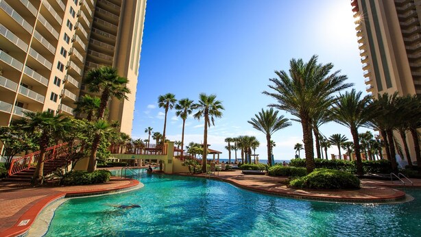 A swimming pool surrounded by palm trees and high-rise buildings. - Shores Of Panama 1426 1 Bd+bunk Room, Sleeps 6. Renovated! Sunset View! Free Fun! 1 Bedroom Condo by RedAwning (Panama City Beach)